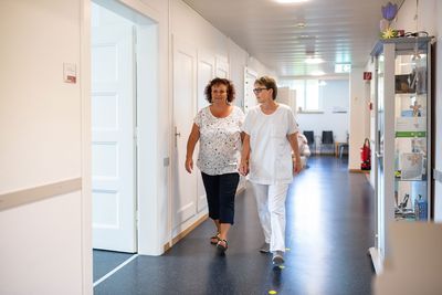 Eine Patientin und eine Mitarbeiterin gehen den Gang entlang