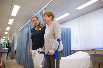 Die Physiotherapeutin begleitet eine Patientin in Krücken