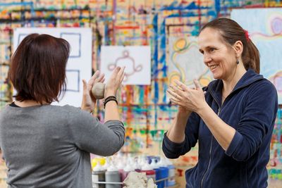 Zwei Frauen formen eine Knetmasse, im Hintergrund sind Bilder zu sehen